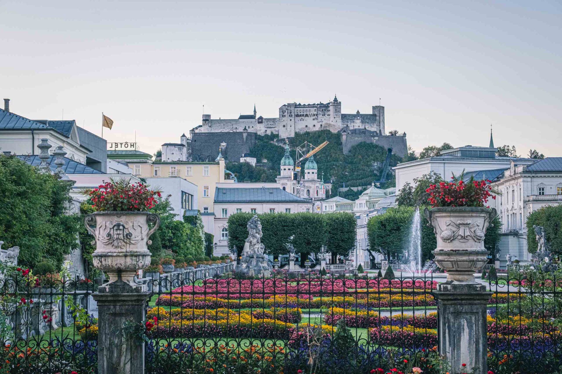 Mirabellgarten mit Blumenbeeten, Statuen und Springbrunnen im Vordergrund und der Festung Hohensalzburg auf einem Hügel im Hintergrund in Salzburg, Österreich.