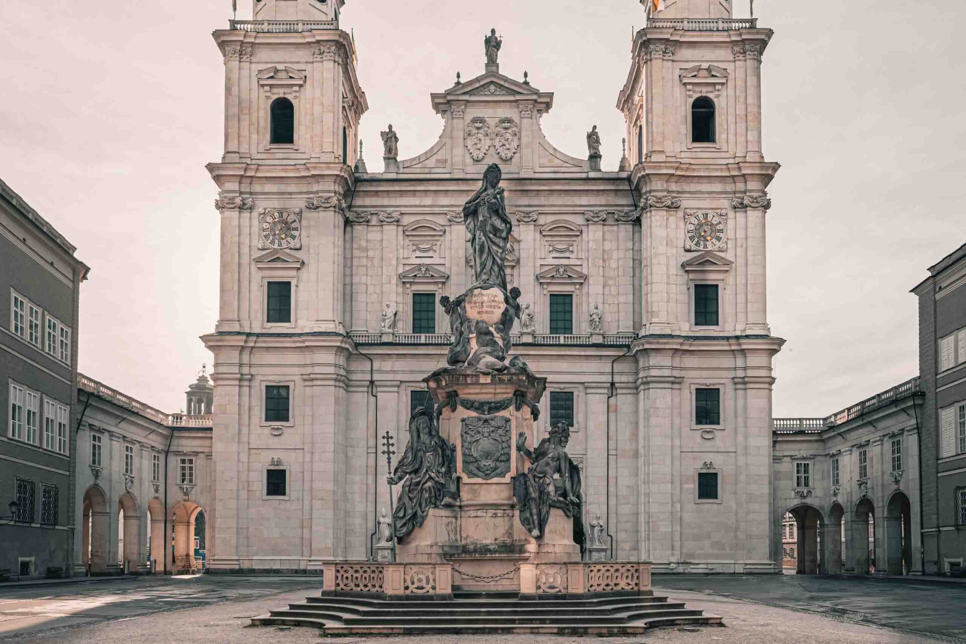 Eine große Steinstatue steht in der Mitte eines Hofes vor einer kunstvollen, historischen Kathedrale mit Zwillingstürmen und Bogenfenstern.