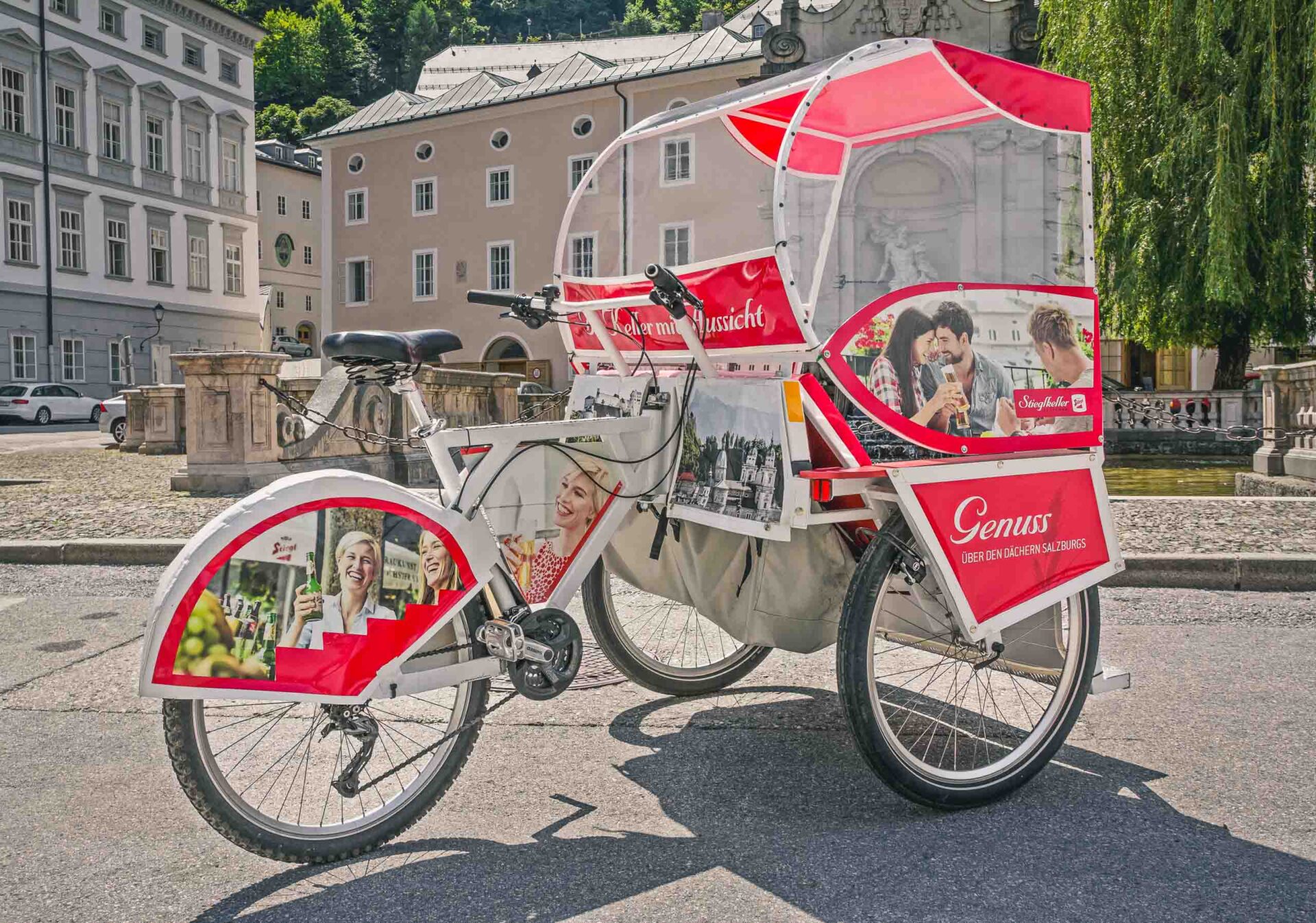 Ein weiß-rotes Fahrradtaxi mit Werbegrafik ist auf einer Kopfsteinpflasterstraße vor historischen europäischen Gebäuden geparkt.